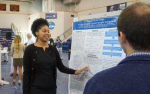 young African - American woman presenting scientific findings from a large poster at a symposium