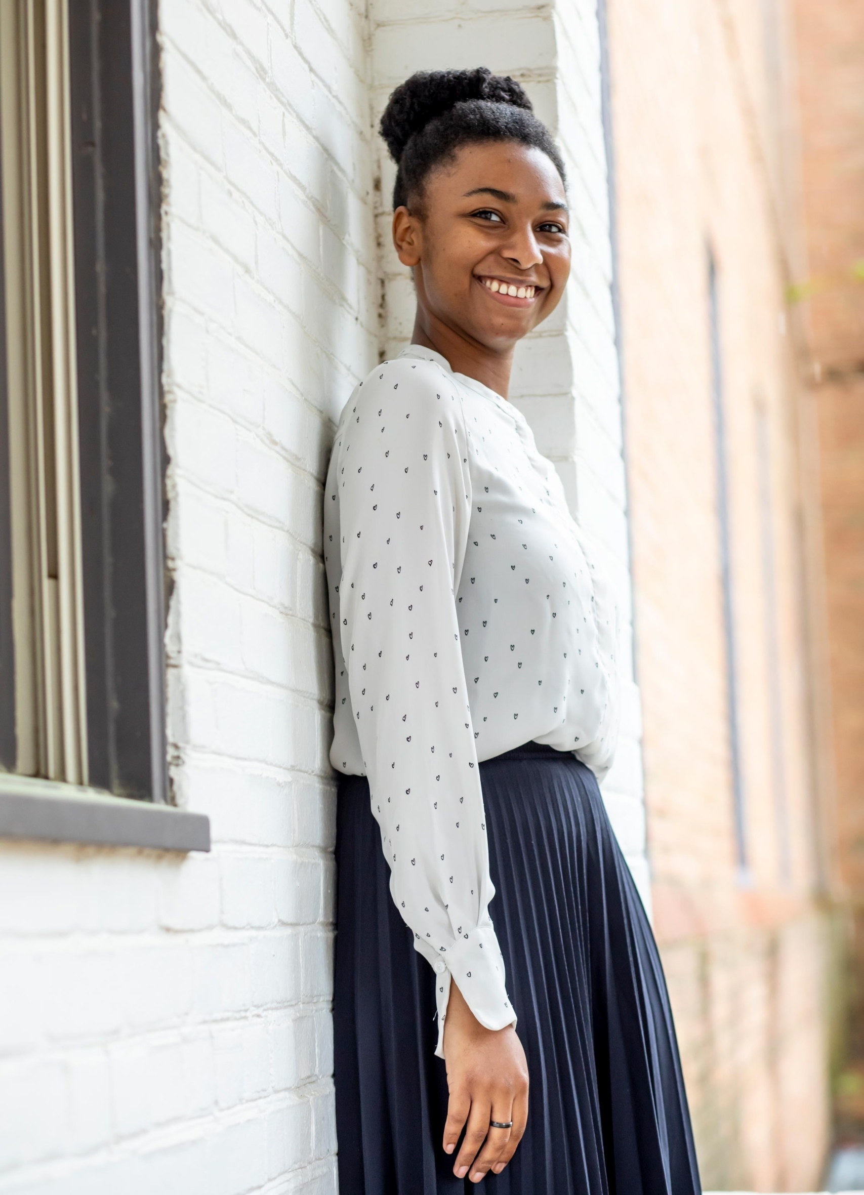 A confident looking woman dressed professionally leans against a brick wall