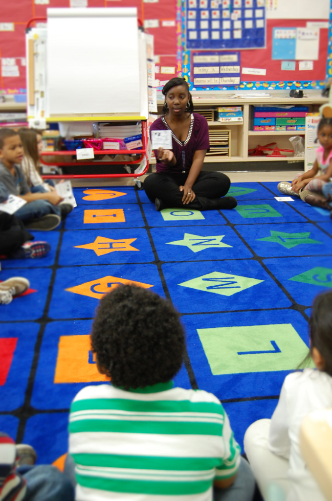 Students sit in a circle and the student teacher holds something up for the class to see