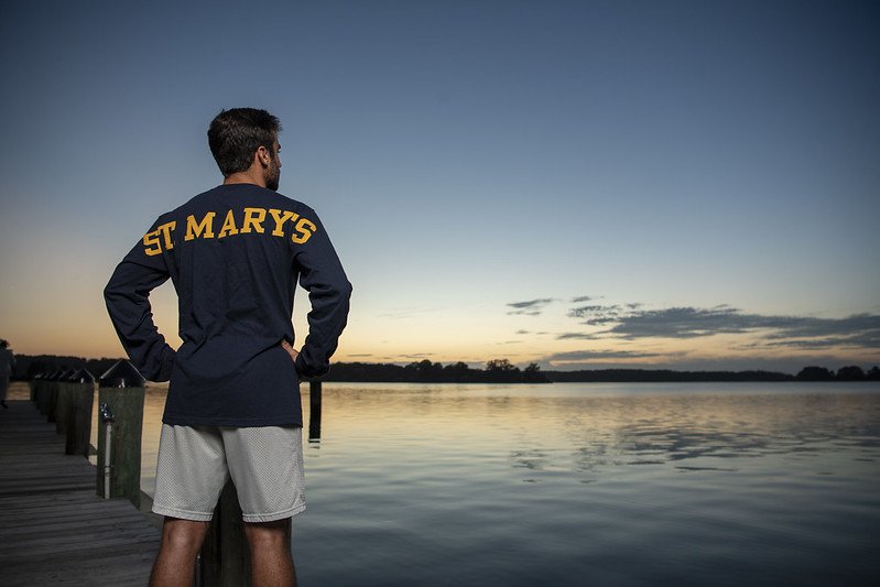 Student wearing St. Mary's logo shirt facing away from the camera, looking towards the water