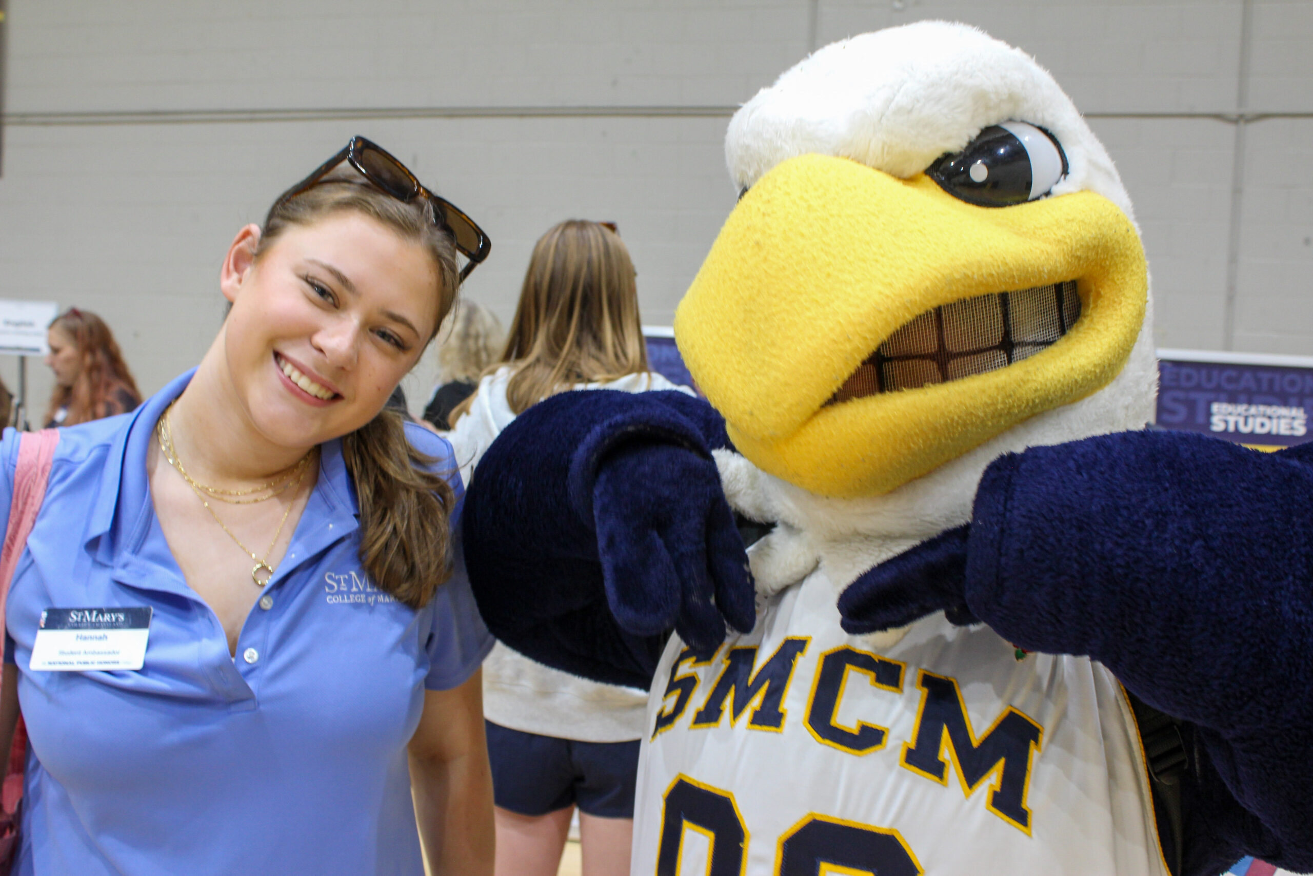 A smiling student wearing a St. Mary’s College of Maryland polo shirt posing with the school’s eagle mascot.