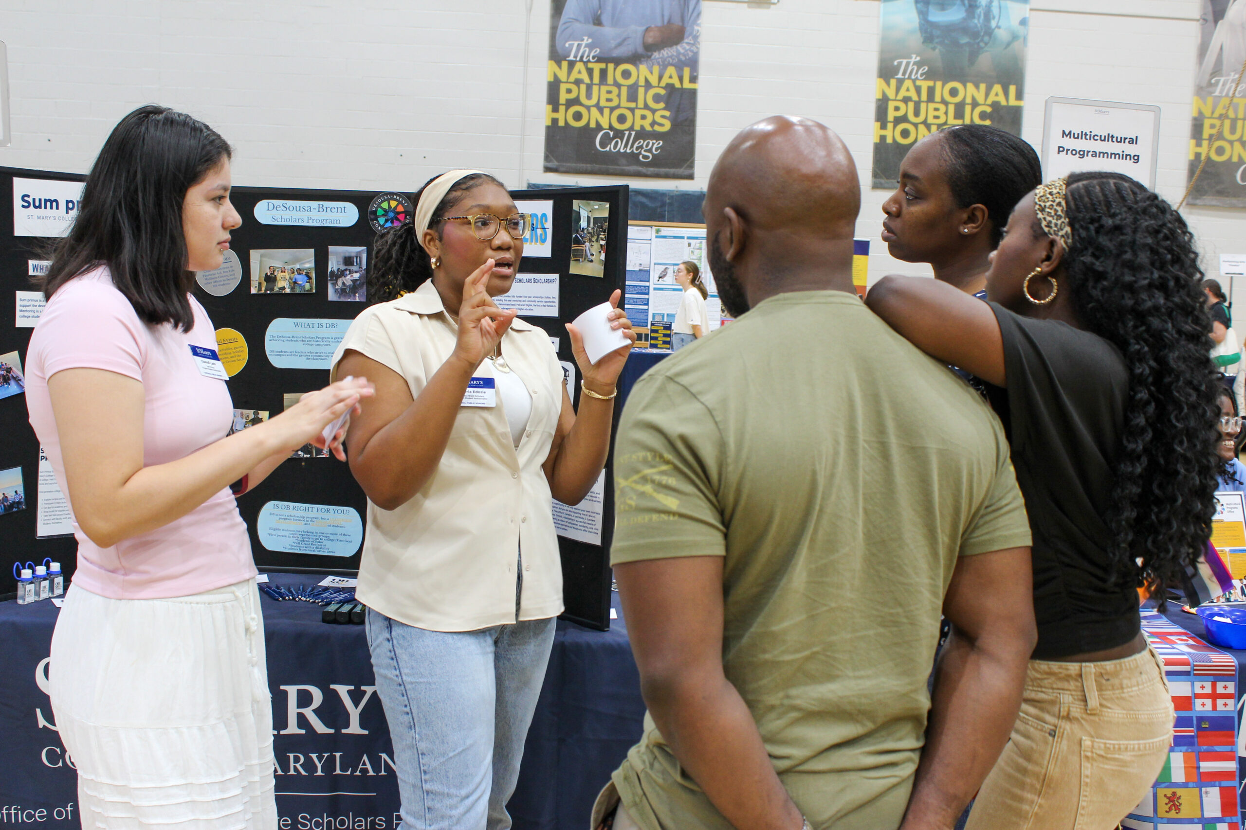 Four people talk around a display board for the DeSousa-Brent Scholars Program at a college fair.