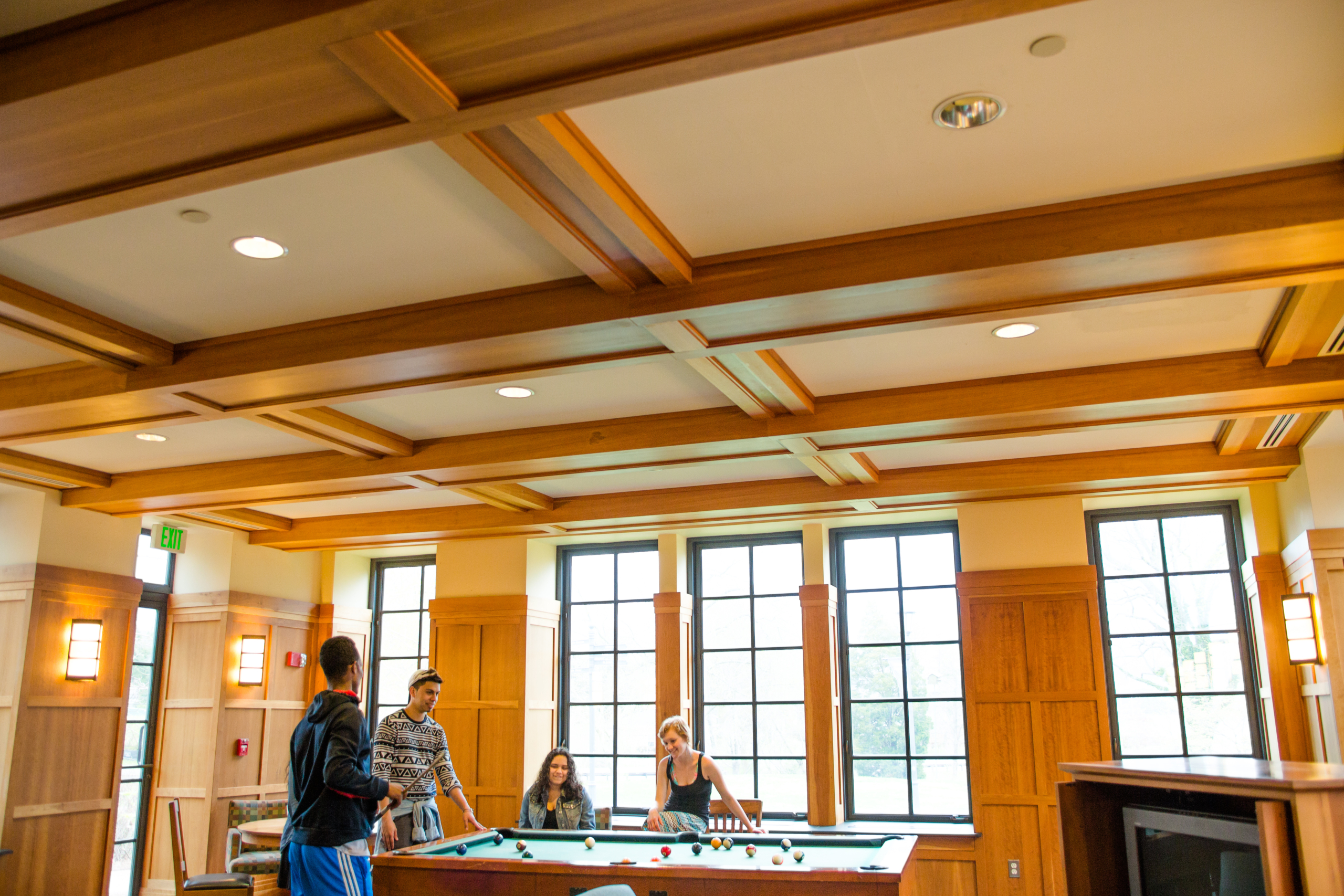 49673042726_43b75184d1_o Four people are gathered around a billiards table in a room with wooden paneling and large windows. The ceiling has a wooden coffered design, and there's a wall-mounted TV on the right.