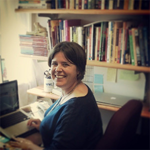 Image of Katy Arnett sitting at a desk with books and a computer in the background.