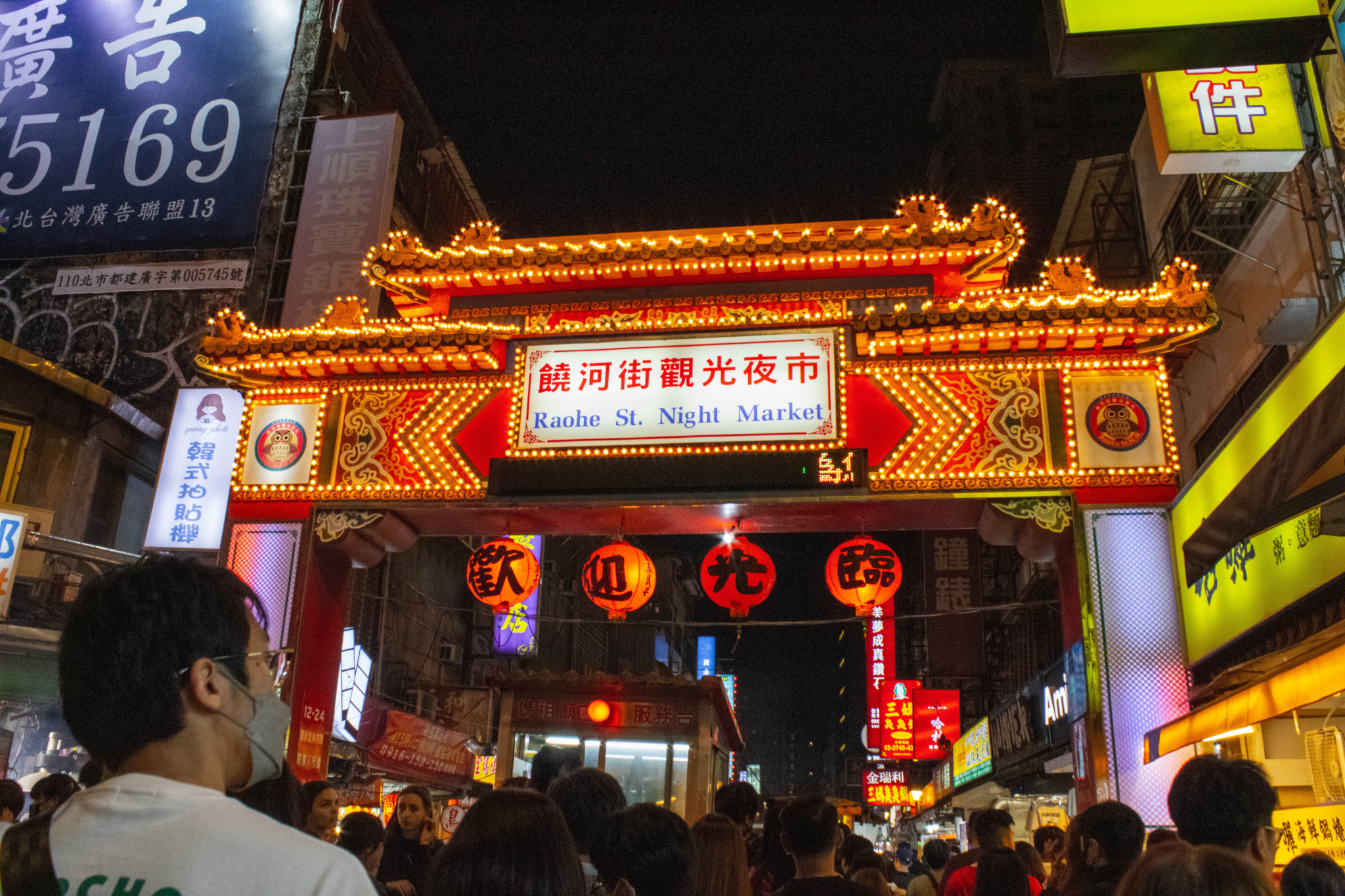 A brightly lit entrance gate to Raohe Street Night Market in Taipei, with crowds of people and illuminated signs at night.