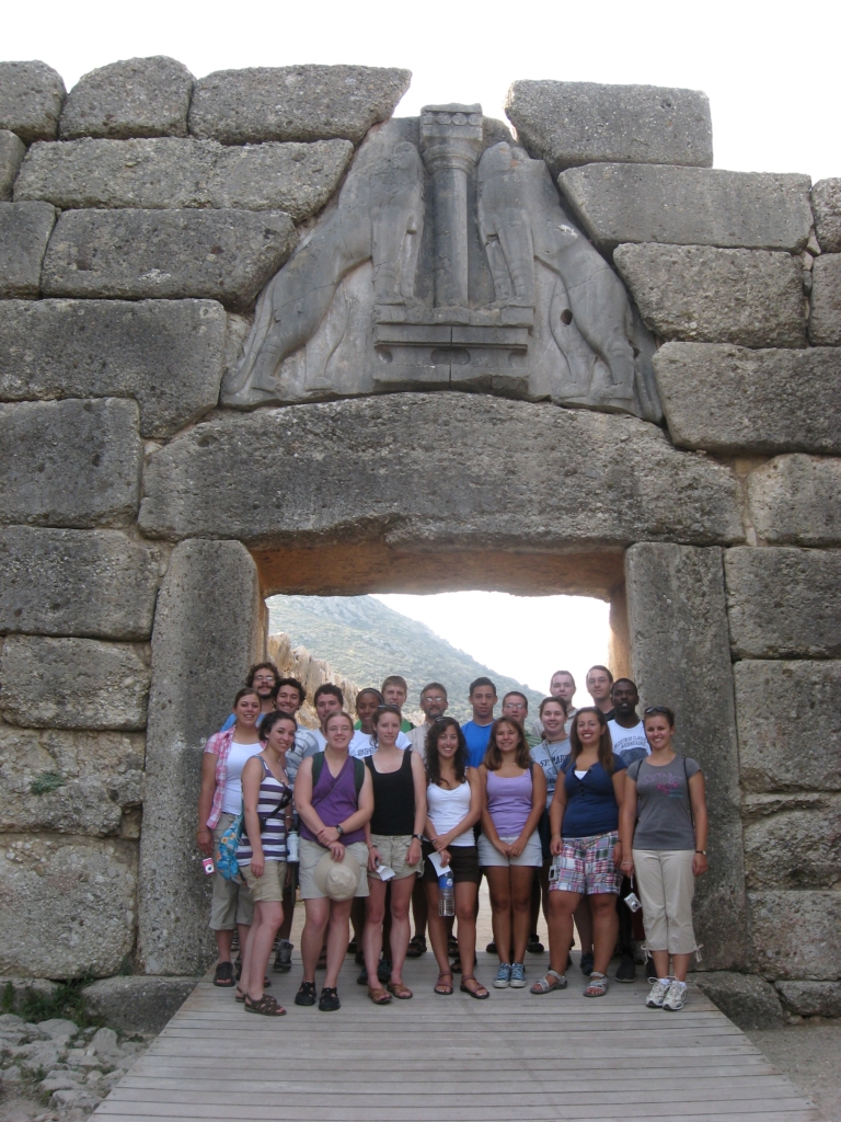 A group of people poses together in front of the ancient stone Lion Gate at Mycenae, Greece.