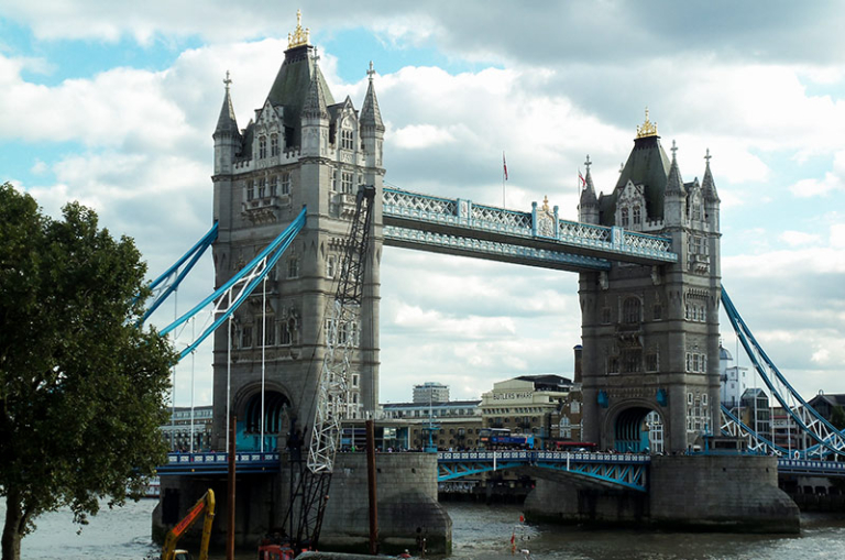 The Tower Bridge in London spans the River Thames, featuring two large towers connected by a pedestrian walkway and suspension elements.