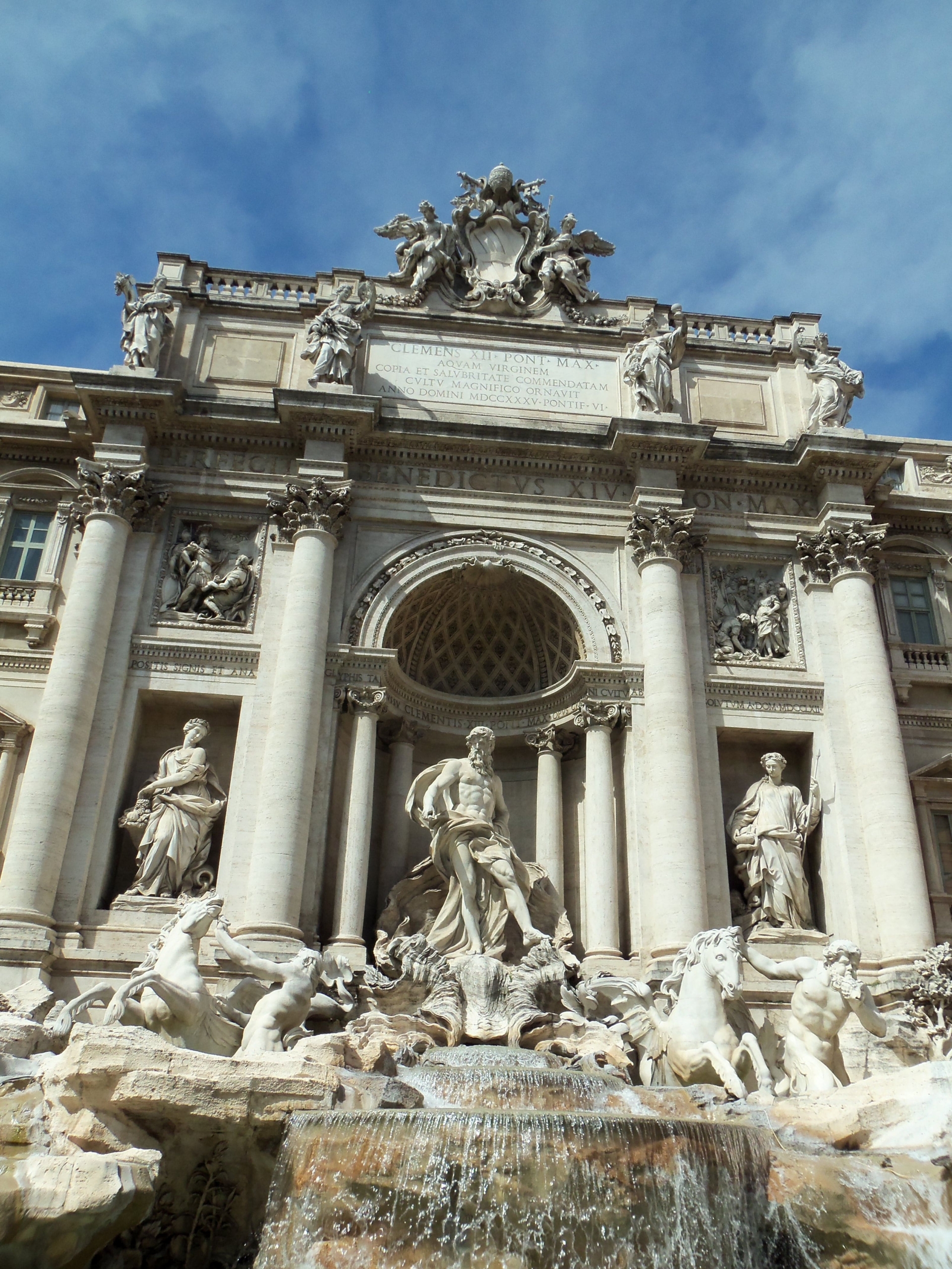 The image shows the Trevi Fountain in Rome, Italy, featuring elaborate sculptures, classical columns, and water cascading at the base.