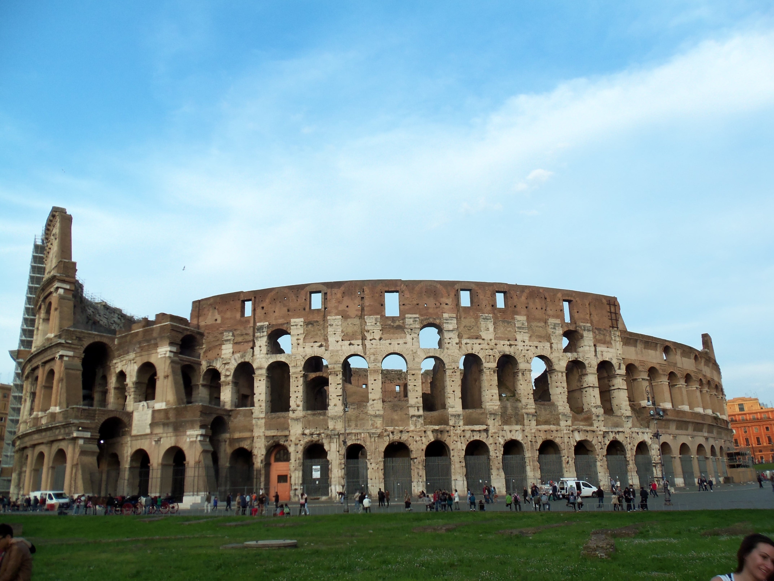 The Colosseum in Rome, Italy, shown on a clear day with tourists gathered around its ancient, partially ruined stone structure.