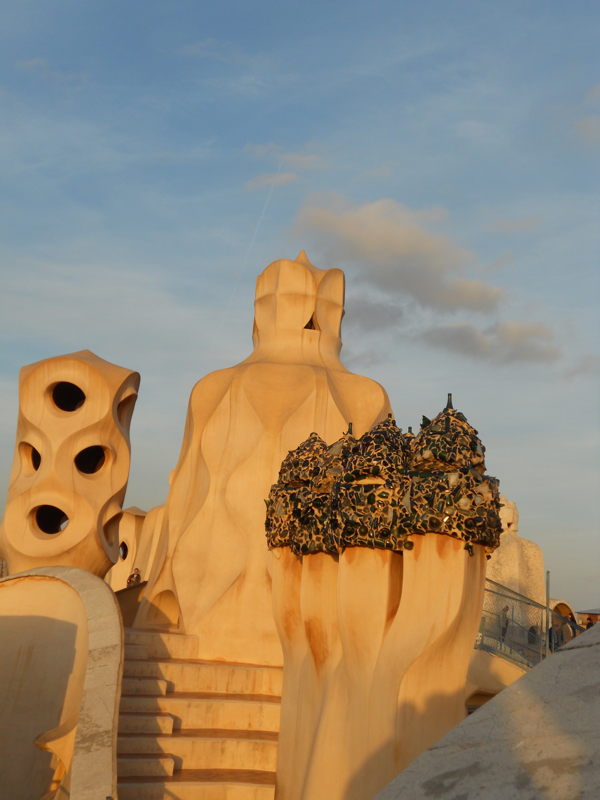 Abstract rooftop chimneys and structures with organic shapes and vents, designed by Antoni Gaudí, are bathed in warm sunlight at Casa Milà in Barcelona.