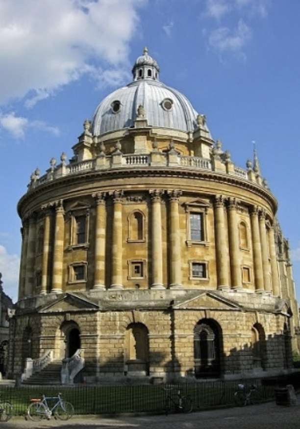 A large, circular stone building with a domed roof and columns, set against a partly cloudy blue sky.