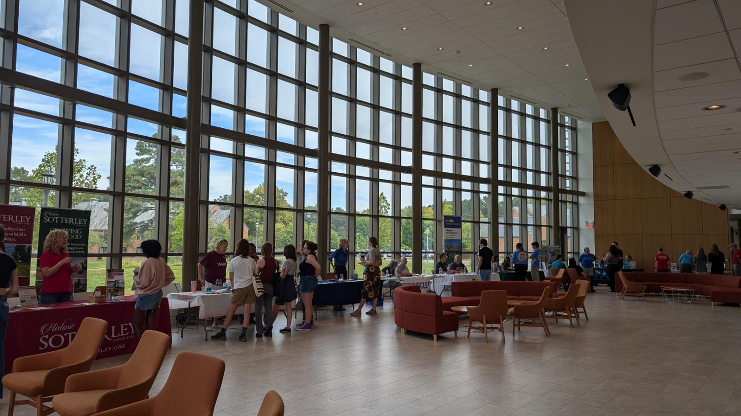 People stand at tables in a spacious, modern lobby with large windows, participating in what appears to be an informational or vendor event.