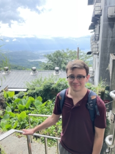 A person with glasses and a backpack stands on stairs, smiling at the camera.