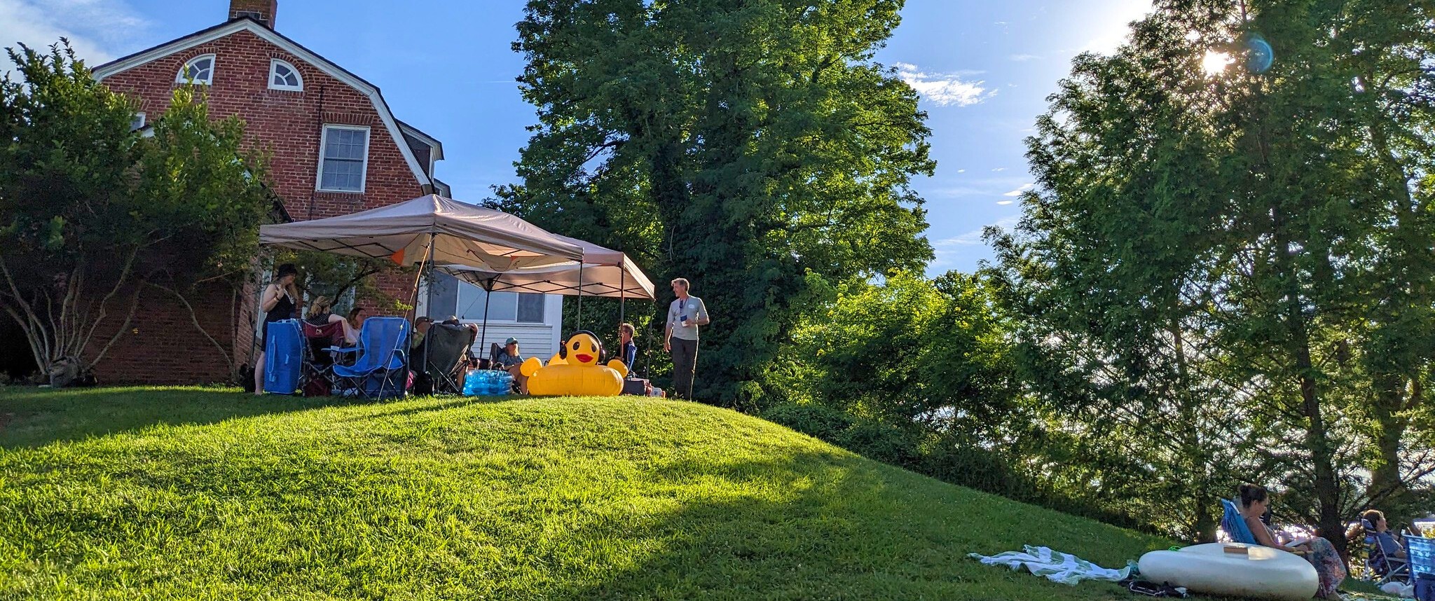 Looking up the hill at the May Russell Alumni Lodge from the James P. Muldoon River Center at a group of savvy alumni set up in style under a pop-up tent and resplendent inflatable inner tube shaped like a classic yellow rubber duck
