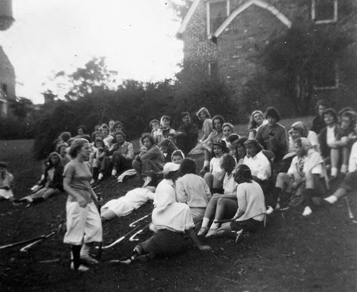 A black and white photo of SMCM students enjoying a chilly day on the hill below the Mary Russell Alumni Lodge, taking a break from field hockey