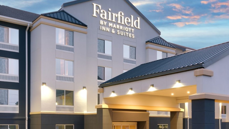 The exterior of a Fairfield by Marriott Inn & Suites hotel, showing its entrance and illuminated signage at sunset.