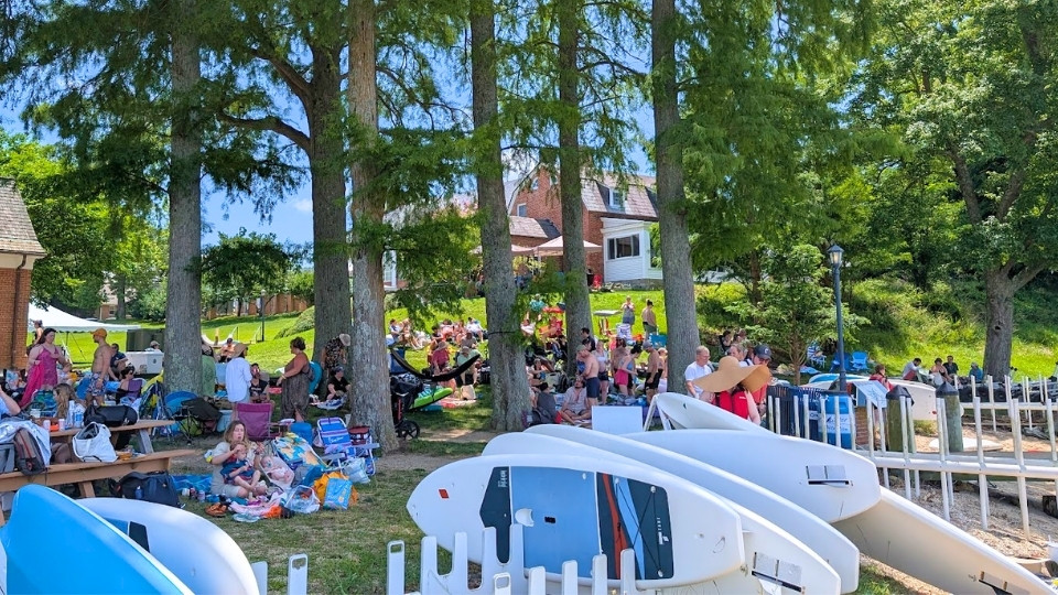 The crowd gathers under the trees at the waterfront during Alumni Weekend