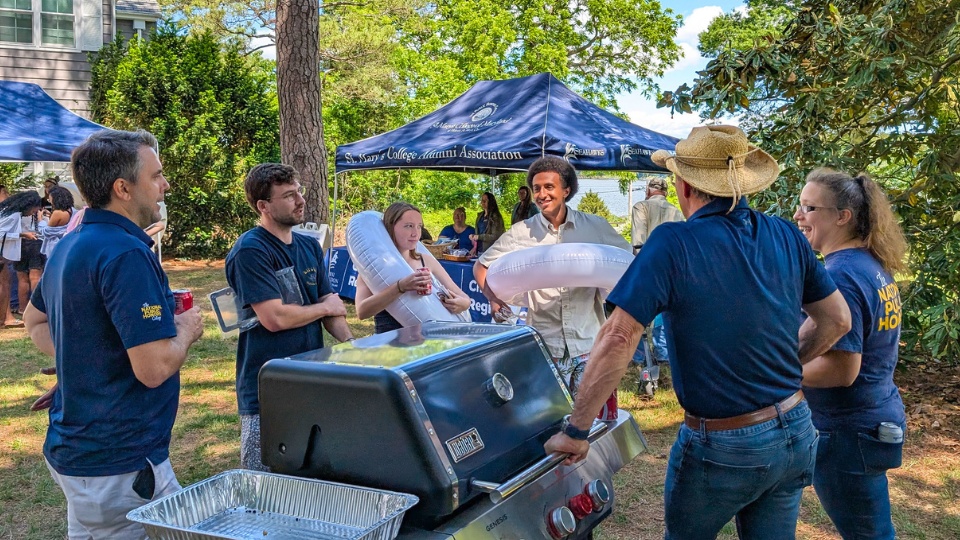 SMCM Almost Alumni Cookout 2025 - the grill team chats while they wait on the next batch of patties to cook