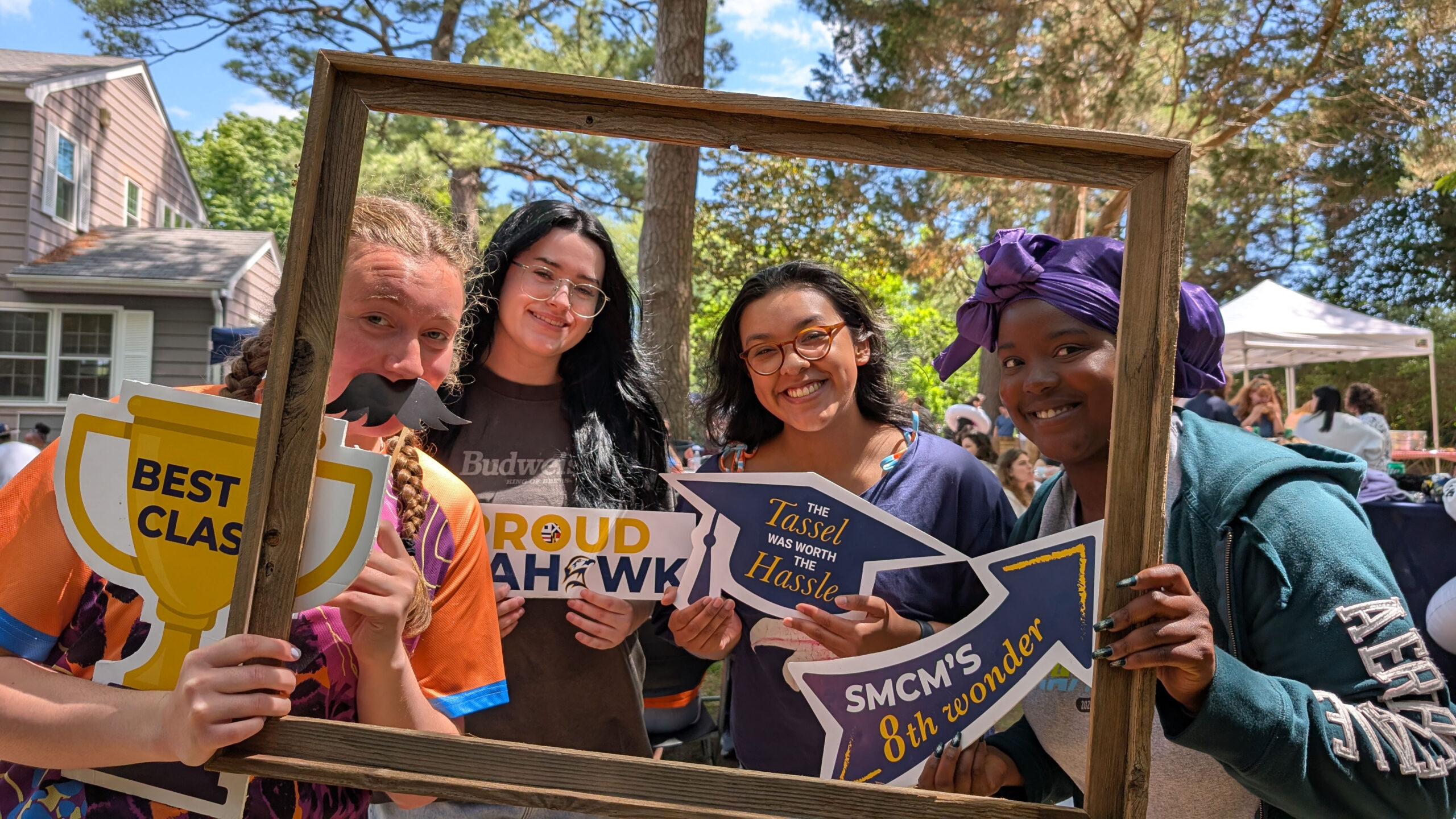 Class of 2026 SMCM seniors pose with graduation props and picture frame at the Almost Alumni Cookout