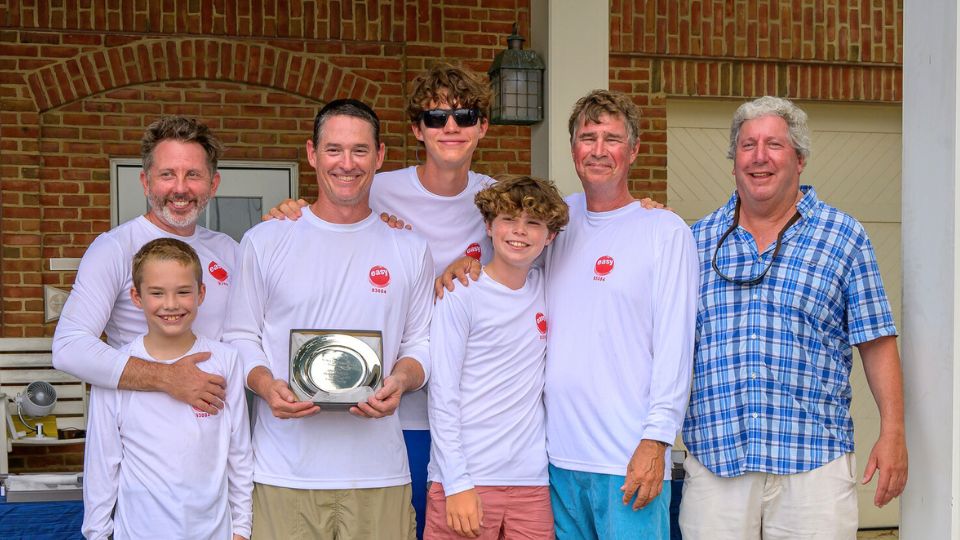 Seven men and boys pose together, six wearing matching white shirts; one man holds a silver plate award in front of a brick wall background. Adam Werblow