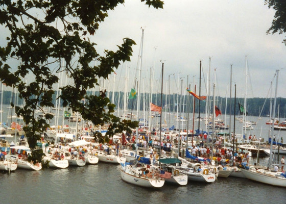 Dozens of sailboats docked side by side at a marina, with many people gathered on the boats and docks; trees frame the top of the image. Governor's Cup, 1989