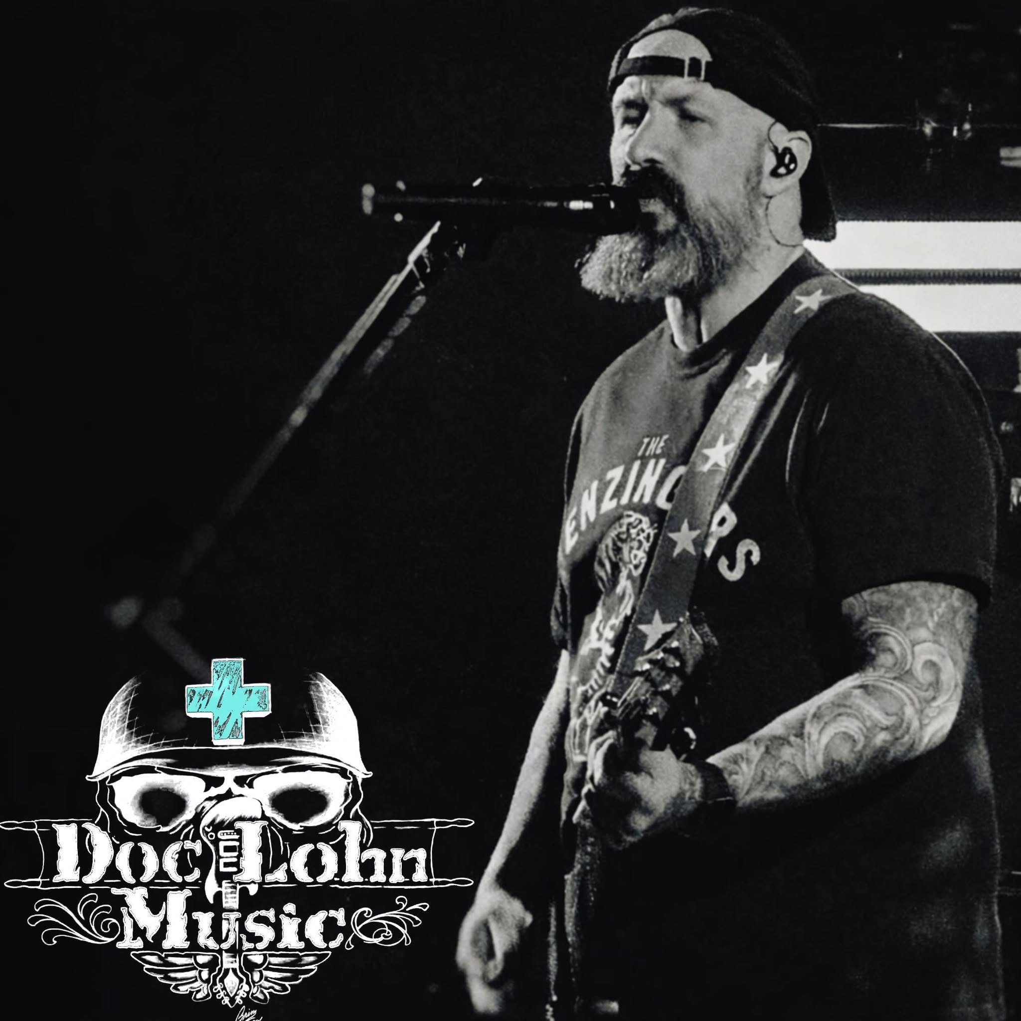 A bearded man with tattoos plays guitar and sings into a microphone on stage. The words "Doc John Music" appear in the bottom left corner of the image.