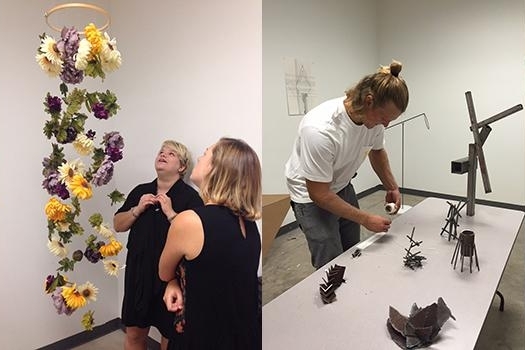 artCapstone Two women observe a hanging floral art piece, while a man works on assembling small metal sculptures on a table in an art studio.