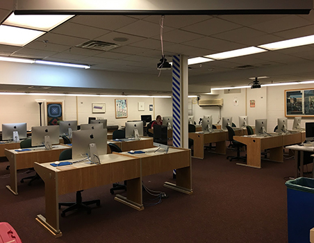digitalLabCombo A computer lab with multiple rows of desks, each equipped with desktop monitors and chairs, in a well-lit room with framed artwork on the walls.