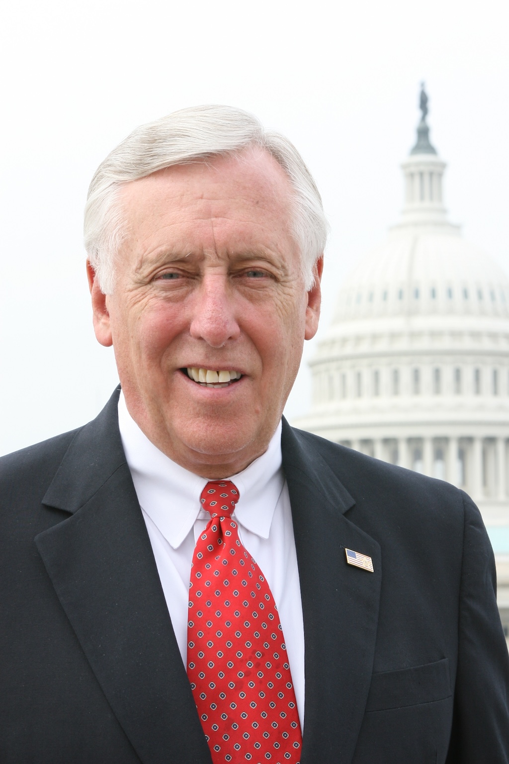 A man in a suit and red patterned tie stands outdoors in front of the U.S. Capitol building.
