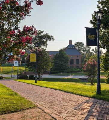 Brick walkway lined with trees leads to a red-brick building; lamp posts display banners for the National Honors Society and St. Mary's College.