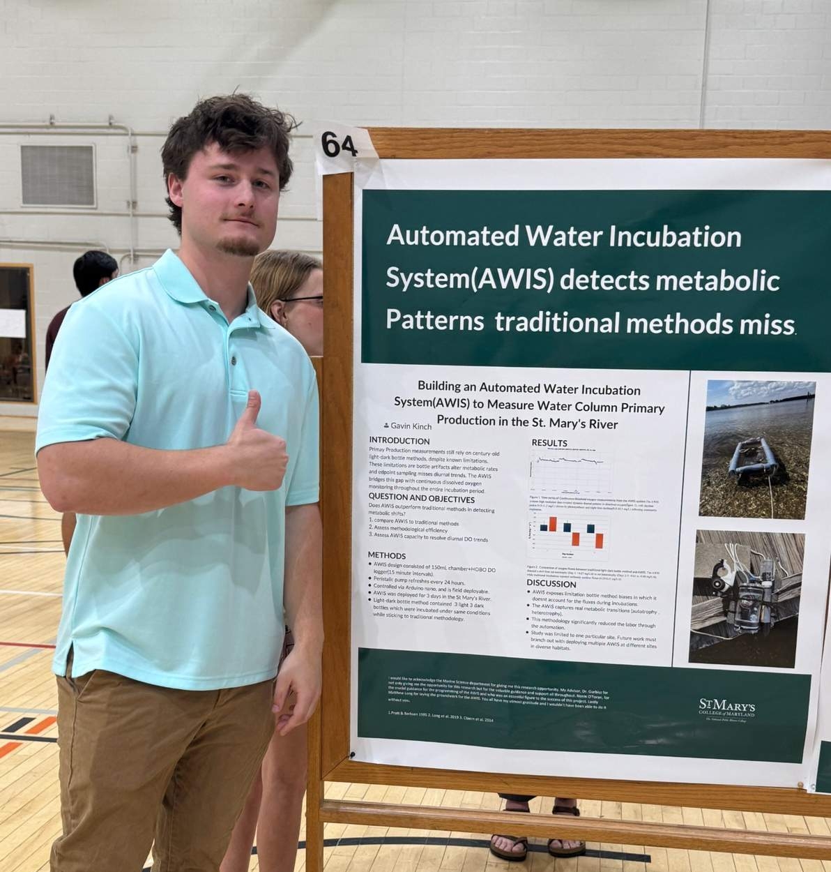 Marine Science SMP A young man stands beside a scientific poster about the Automated Water Incubation System (AWIS) in a gymnasium, giving a thumbs-up gesture.