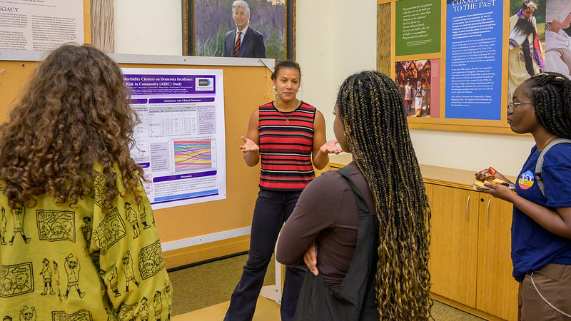 Photo by Chuck Steenburgh A woman stands in front of a research poster, speaking to three other women in a classroom setting with informational displays on the walls.