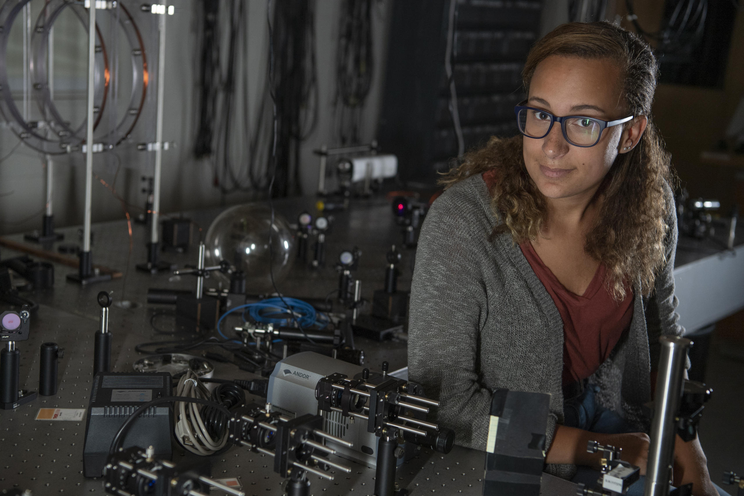 2110-2232 A person with glasses sits at a lab bench surrounded by scientific instruments and optical equipment.