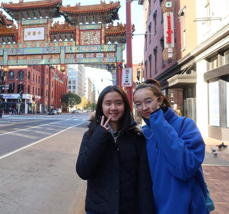 50888884602_2a242d8f4e_o Two young women stand on a city street in front of a traditional Chinese archway, with buildings, a bus, and Walgreens visible in the background.