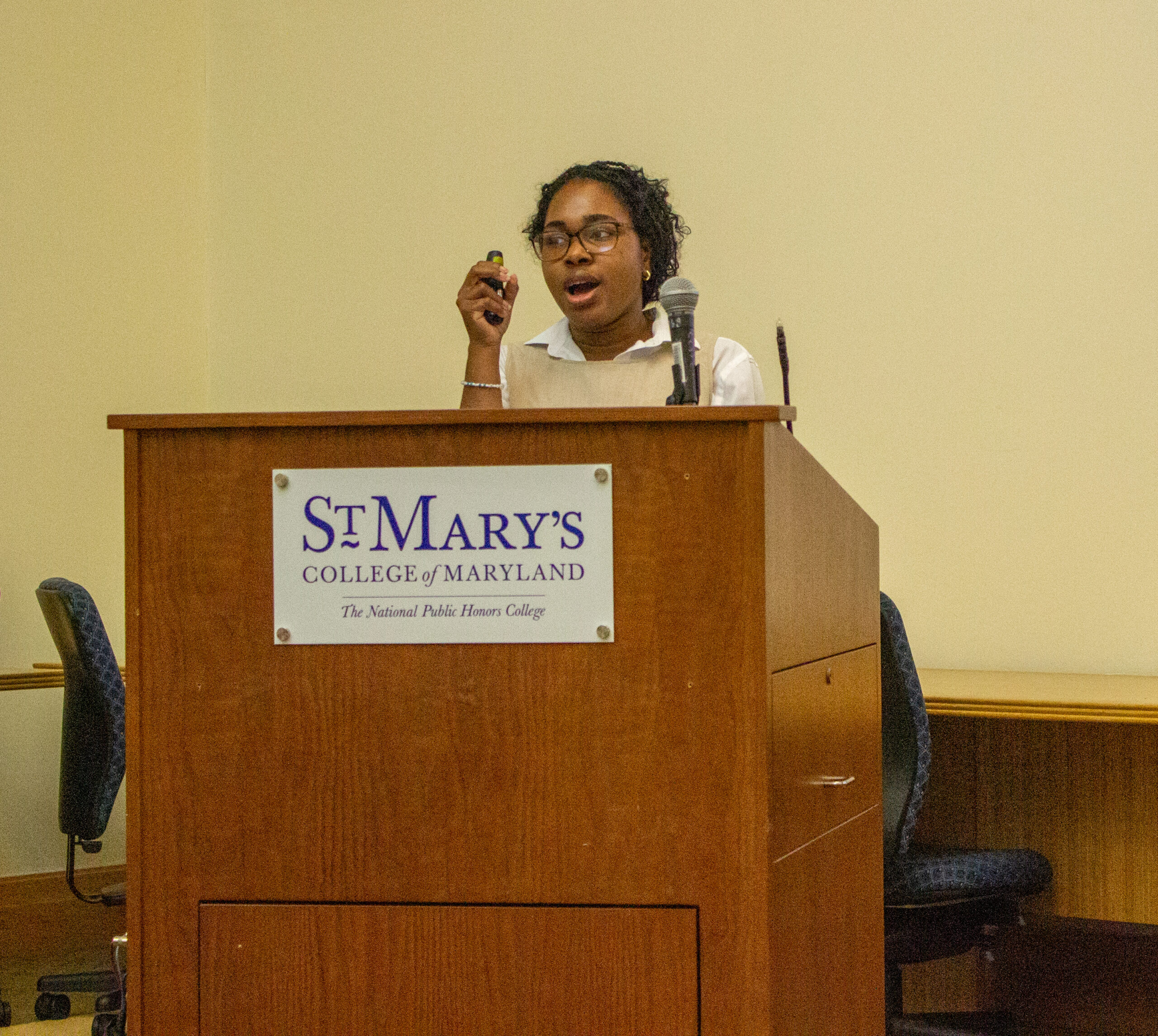 A person stands behind a podium labeled "St. Mary’s College of Maryland," speaking into a microphone and holding a small device.
