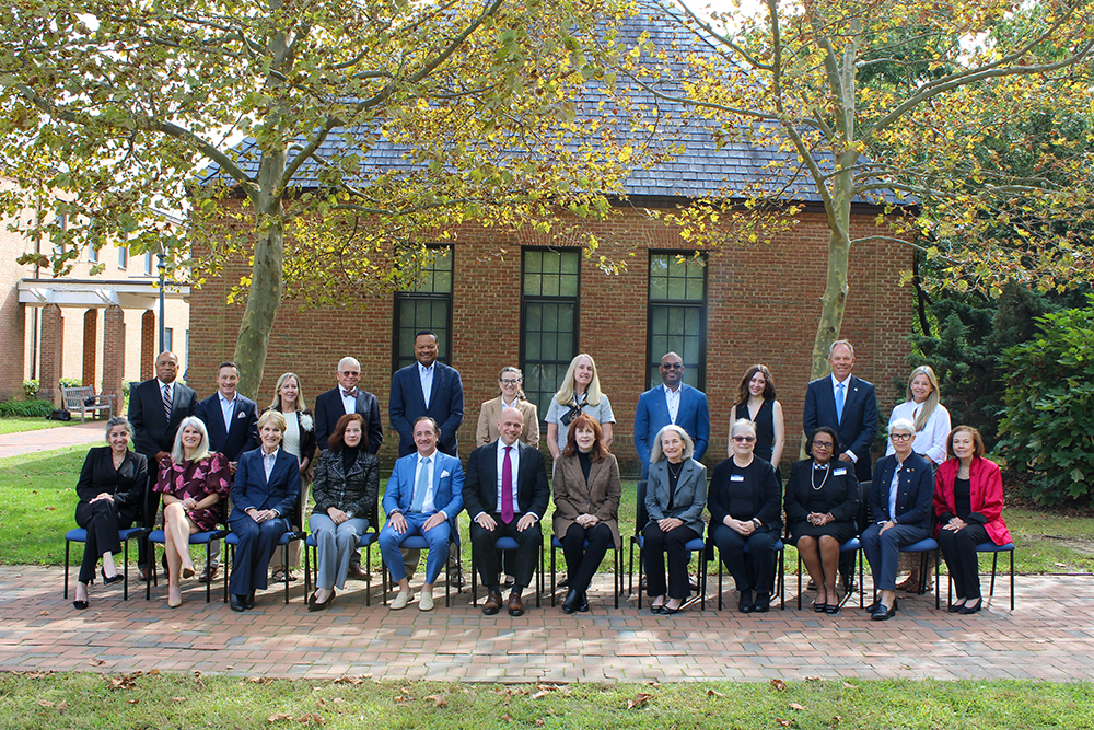 St. Mary's College of Maryland Board of Trustees, a group of twenty-four professionals pose for a group photo in front of a brick building.