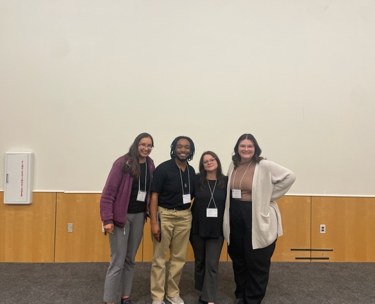 Four people standing side by side with name tags, smiling and posing for a photo.