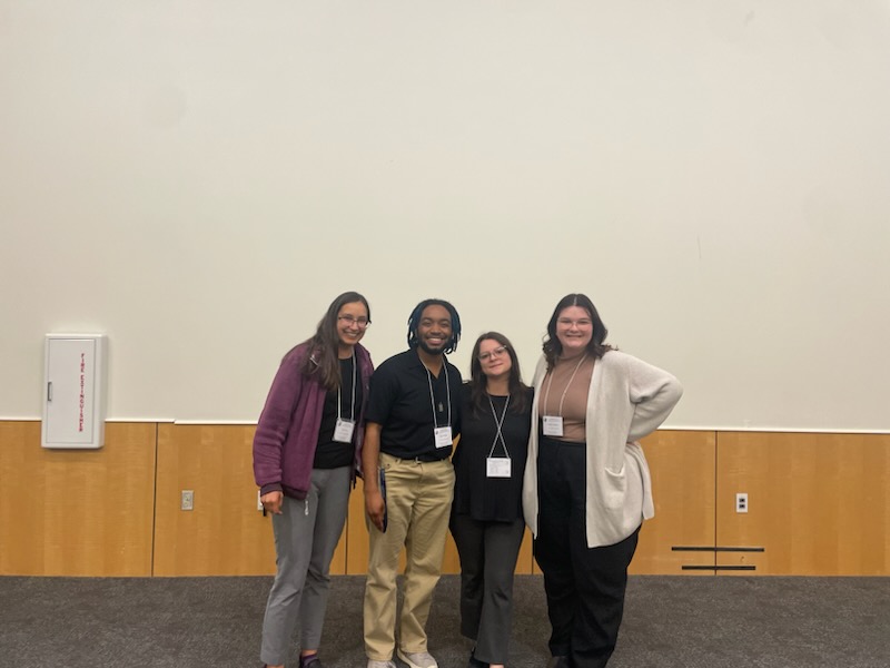 Four people standing side by side with name tags, smiling and posing for a photo.