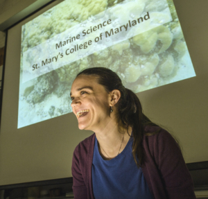 Elizabeth Hamman A person smiling in front of a presentation slide titled "Marine Science, St. Mary's College of Maryland," proudly showcases their achievements and awards in the field.