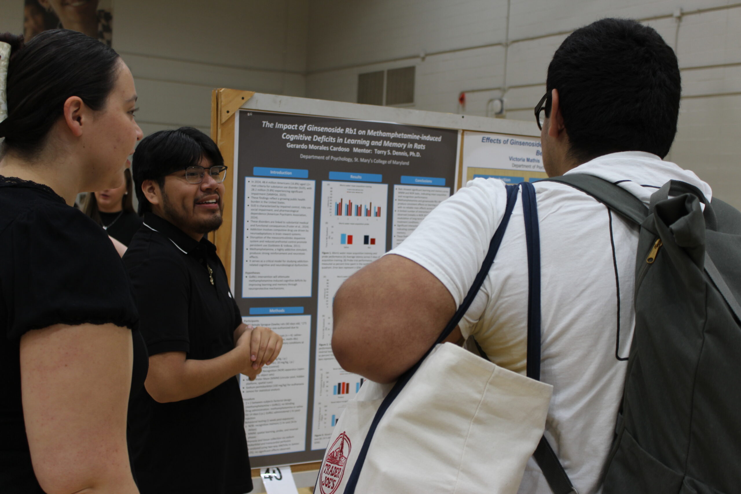 Three people stand in front of a scientific research poster, discussing the displayed graphs and information in an indoor setting.