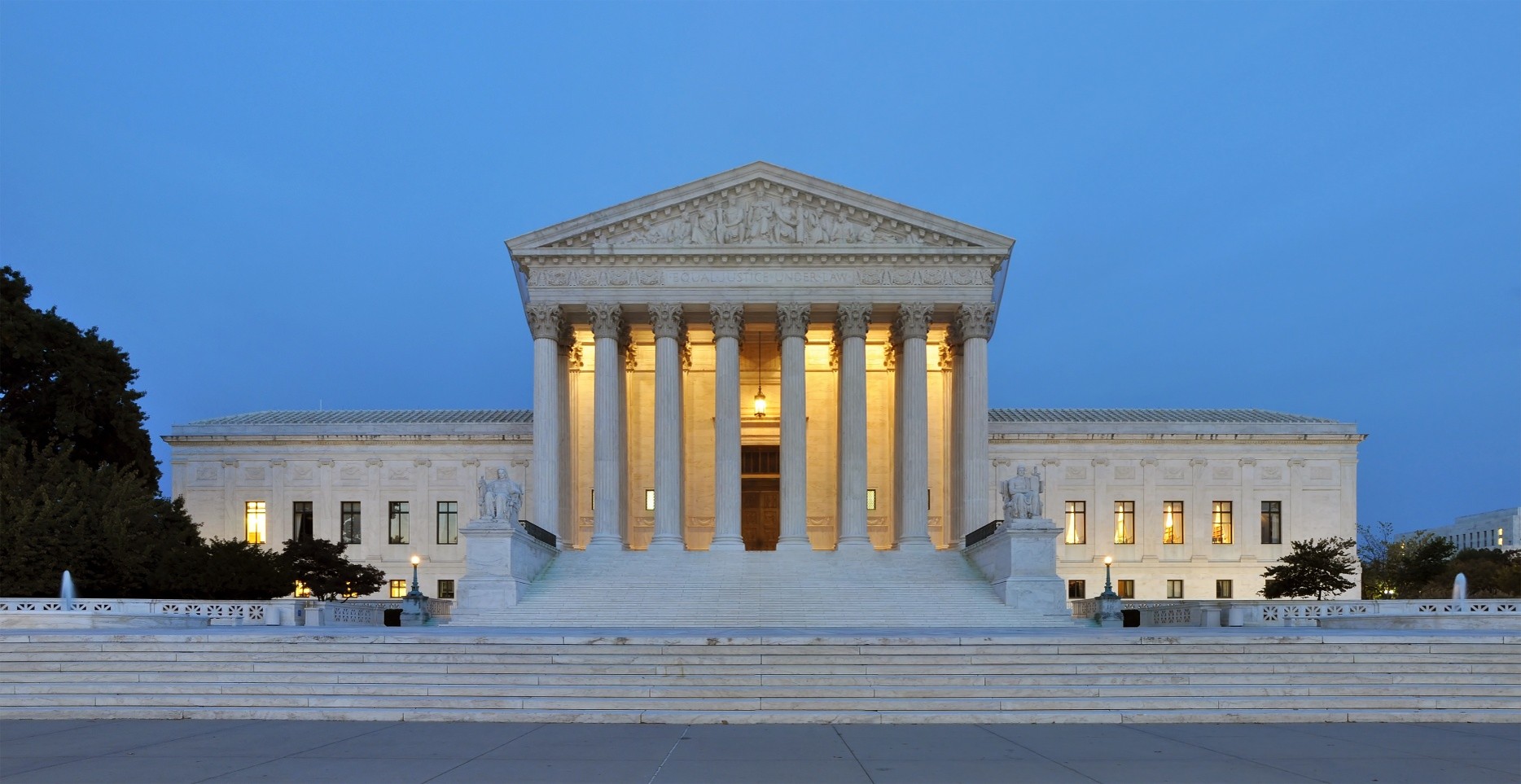 The United States Supreme Court building with illuminated columns at dusk, viewed from the front with steps leading up to the entrance.