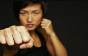 A person focuses intently, holding a fighting stance with a clenched fist extended toward the camera. The background is dark, emphasizing their determination and strength.