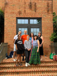 Seven people pose for a group photo on brick steps in front of a large windowed door set in a brick building.