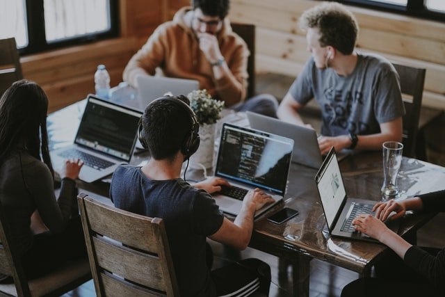 Five students sitting a large table, each using laptops, working and socializing.