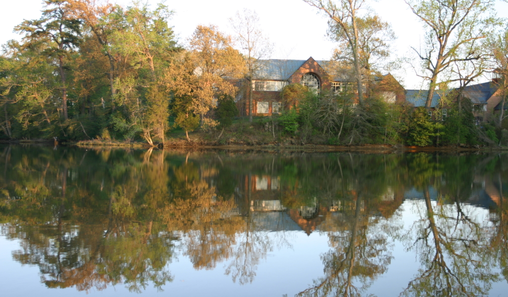 A brick library surrounded by trees overlooks a pond