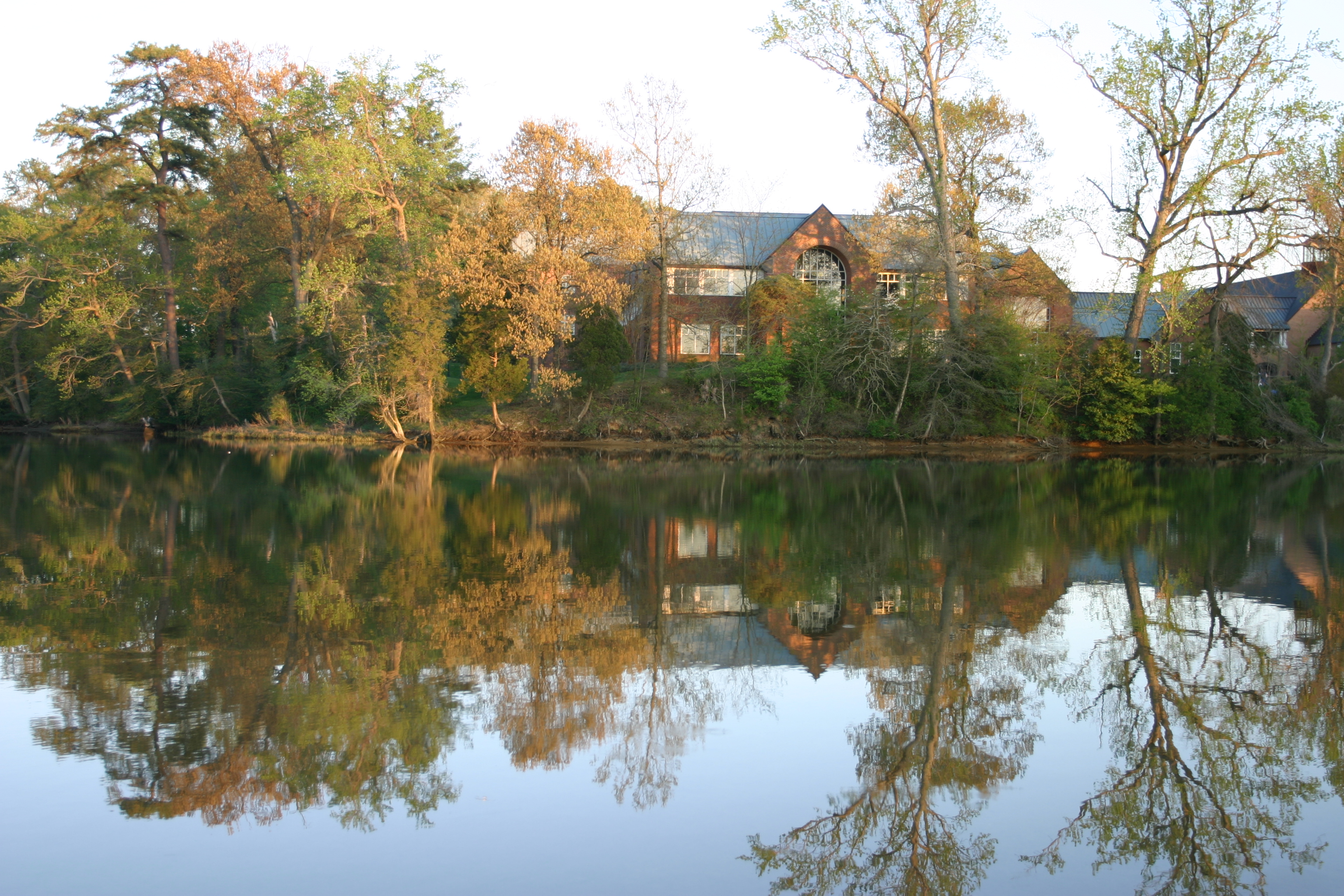 A brick library surrounded by trees overlooks a pond