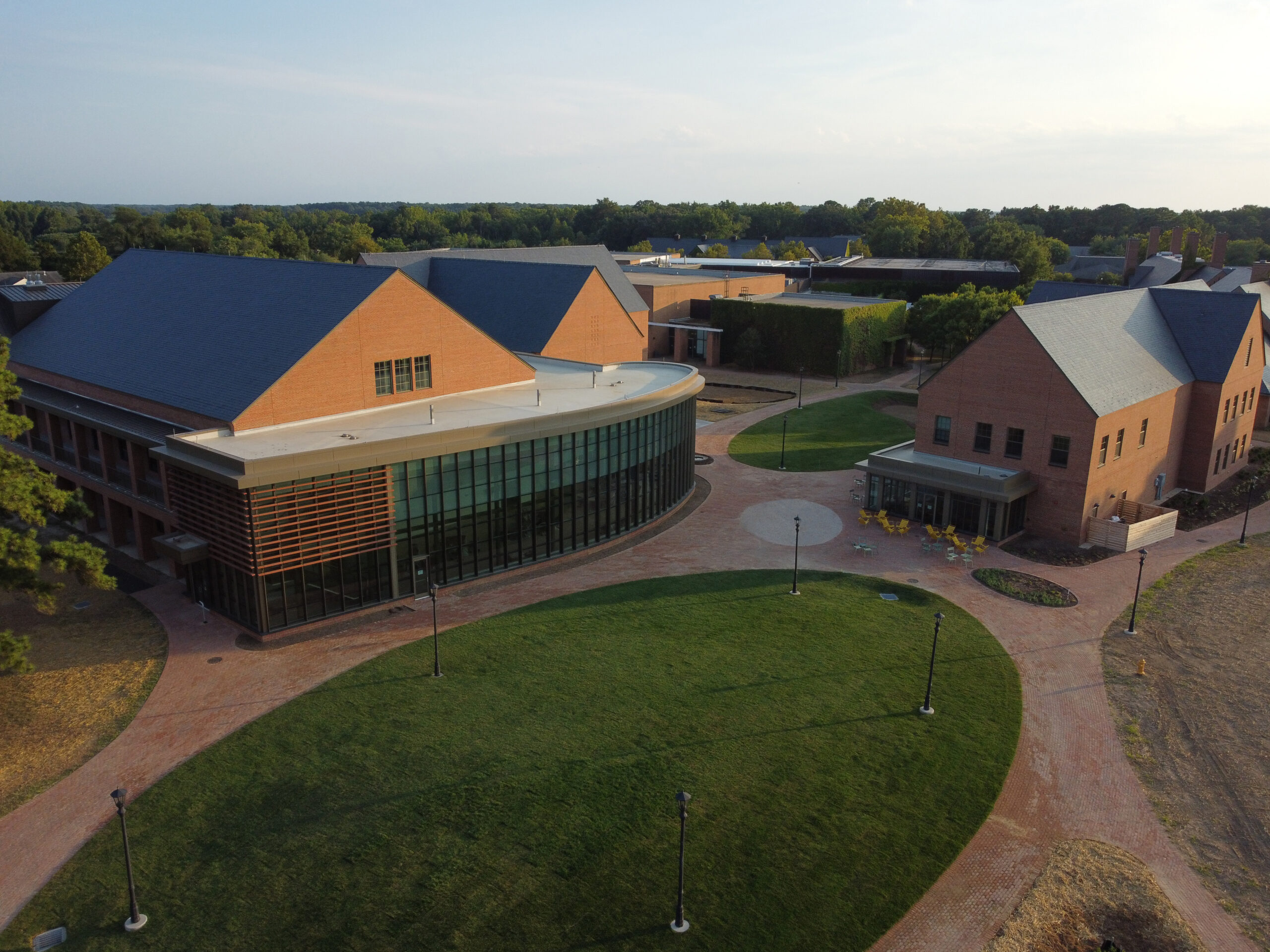 Aerial view of a modern brick academic building with large glass windows, surrounded by walkways and green lawns, set up for a campus event.