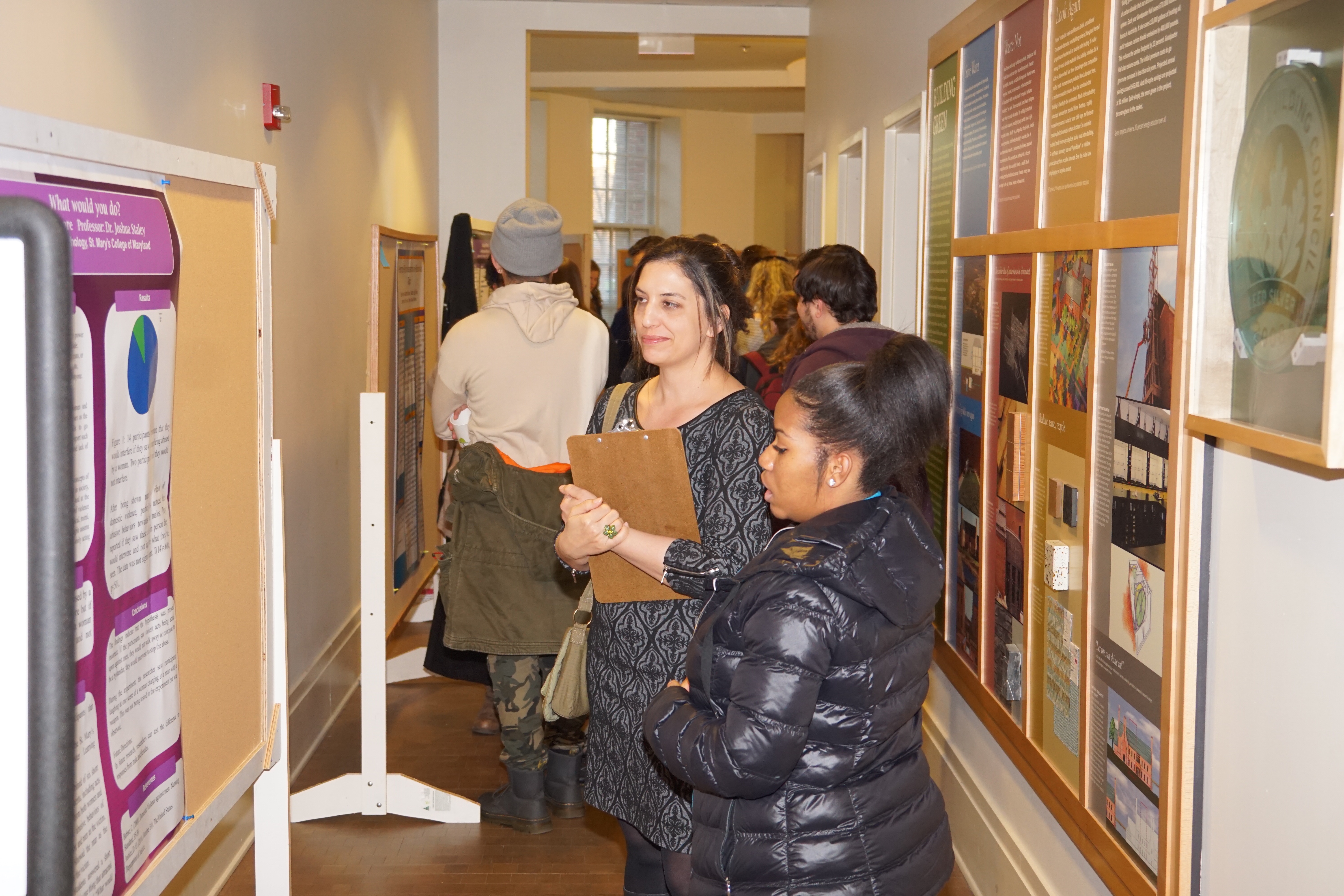 A student standing side-by-side with a teacher who is presenting a project on a billboard