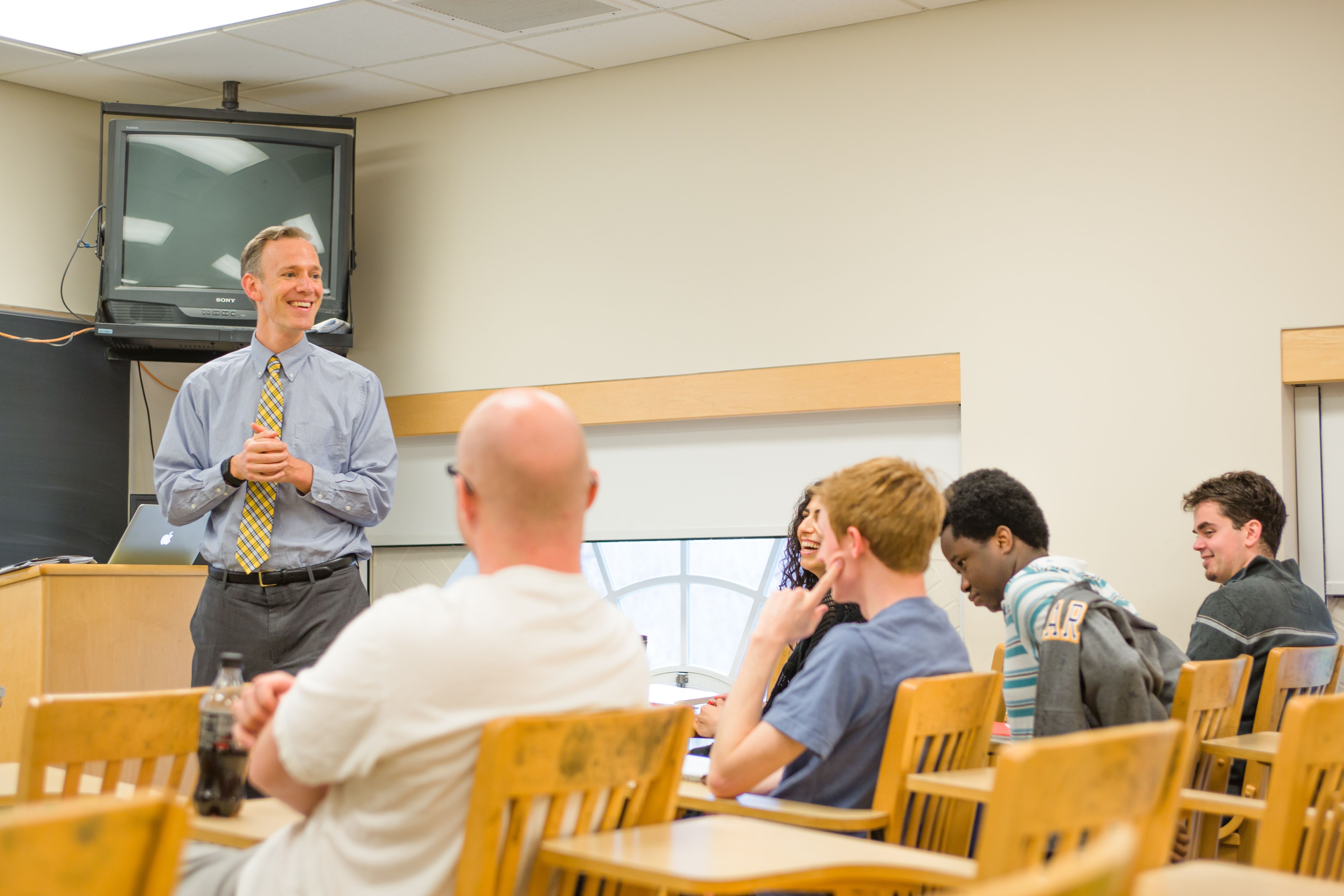 A democracy studies teacher discussing a lesson with a group of students in a classroom