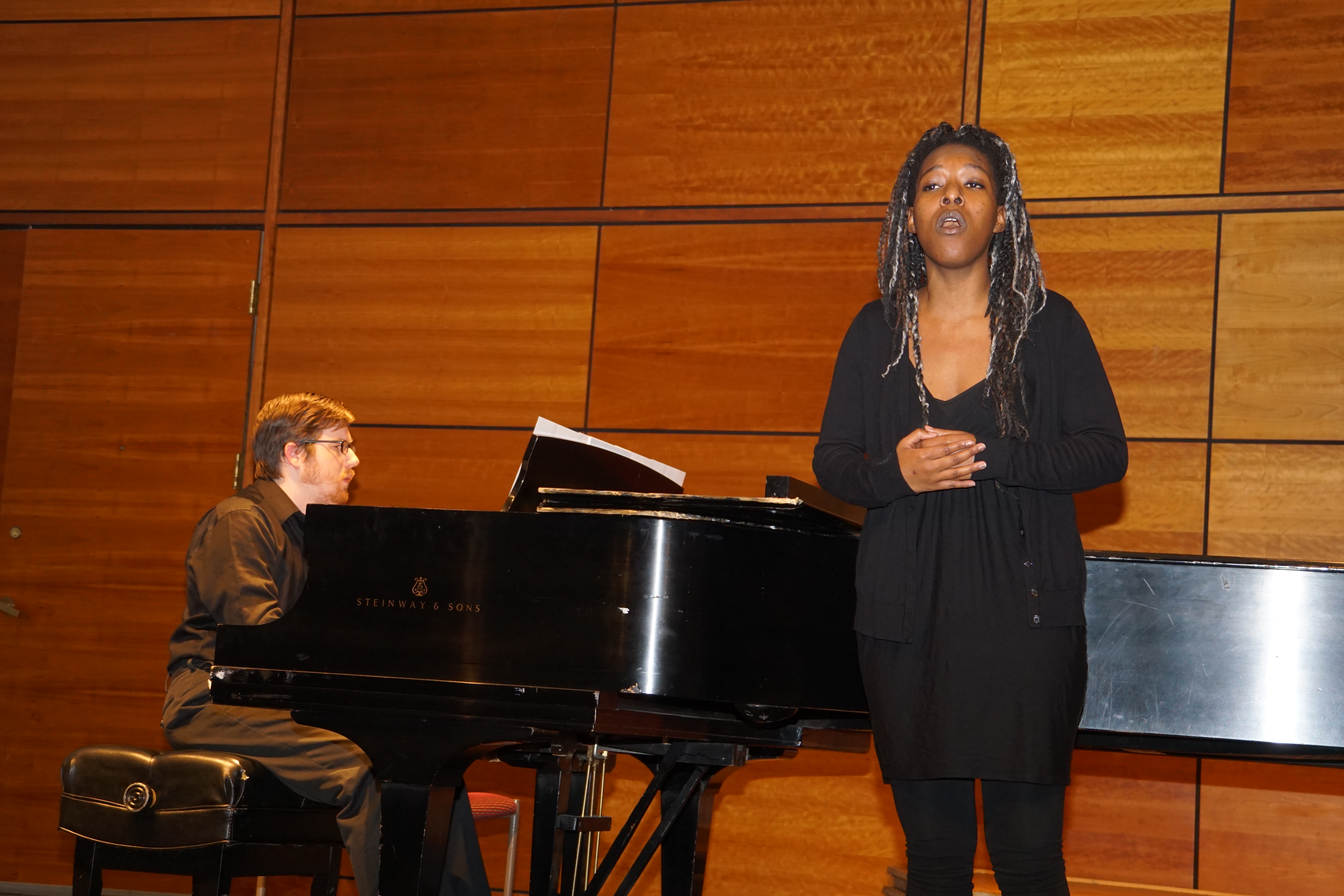 A student singing vocals with an instructor playing piano in the background